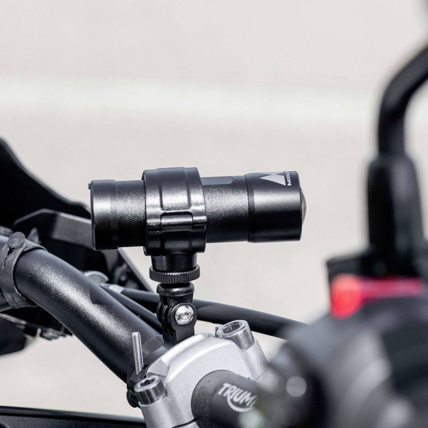 A mounted camera on a motorcycle handlebar in daylight, emphasising the sturdy mounting and forward-facing orientation for video recording.