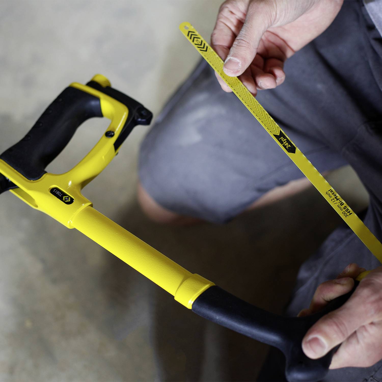 A person is changing the saw blade on a hacksaw. The saw has a yellow frame and the blade is being inserted.