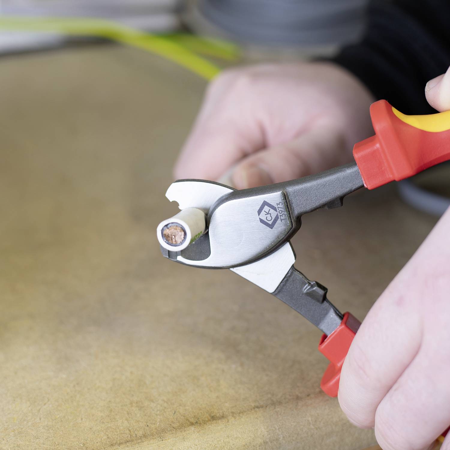 A hand is holding a wire cutter, cutting through a cable. The wire is exposed at the end.