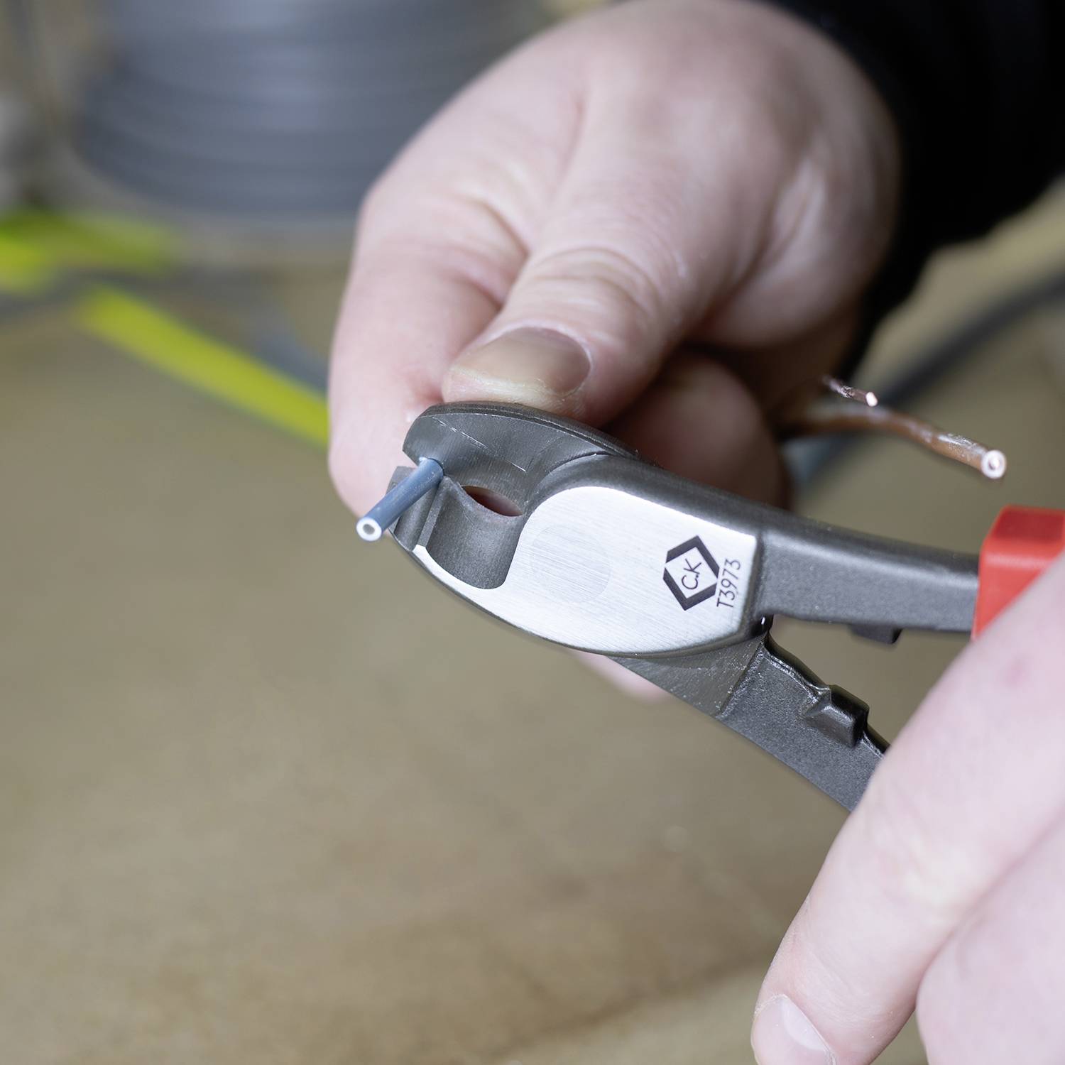 A person is holding a pair of side cutters and cutting a blue cable. The focus is on the hand and the tool.
