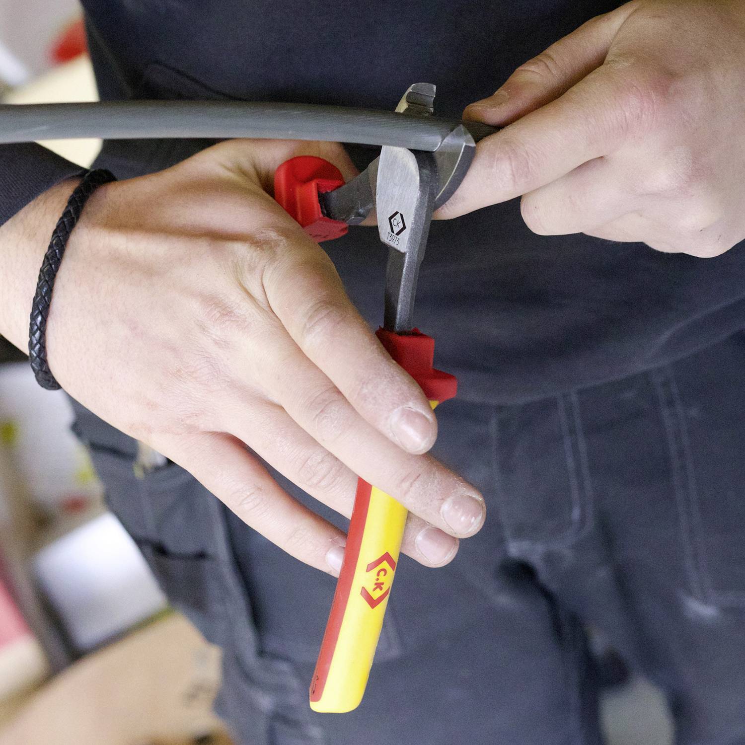 A person is cutting a grey cable with side cutters. Hands are holding tools for cable cutting.