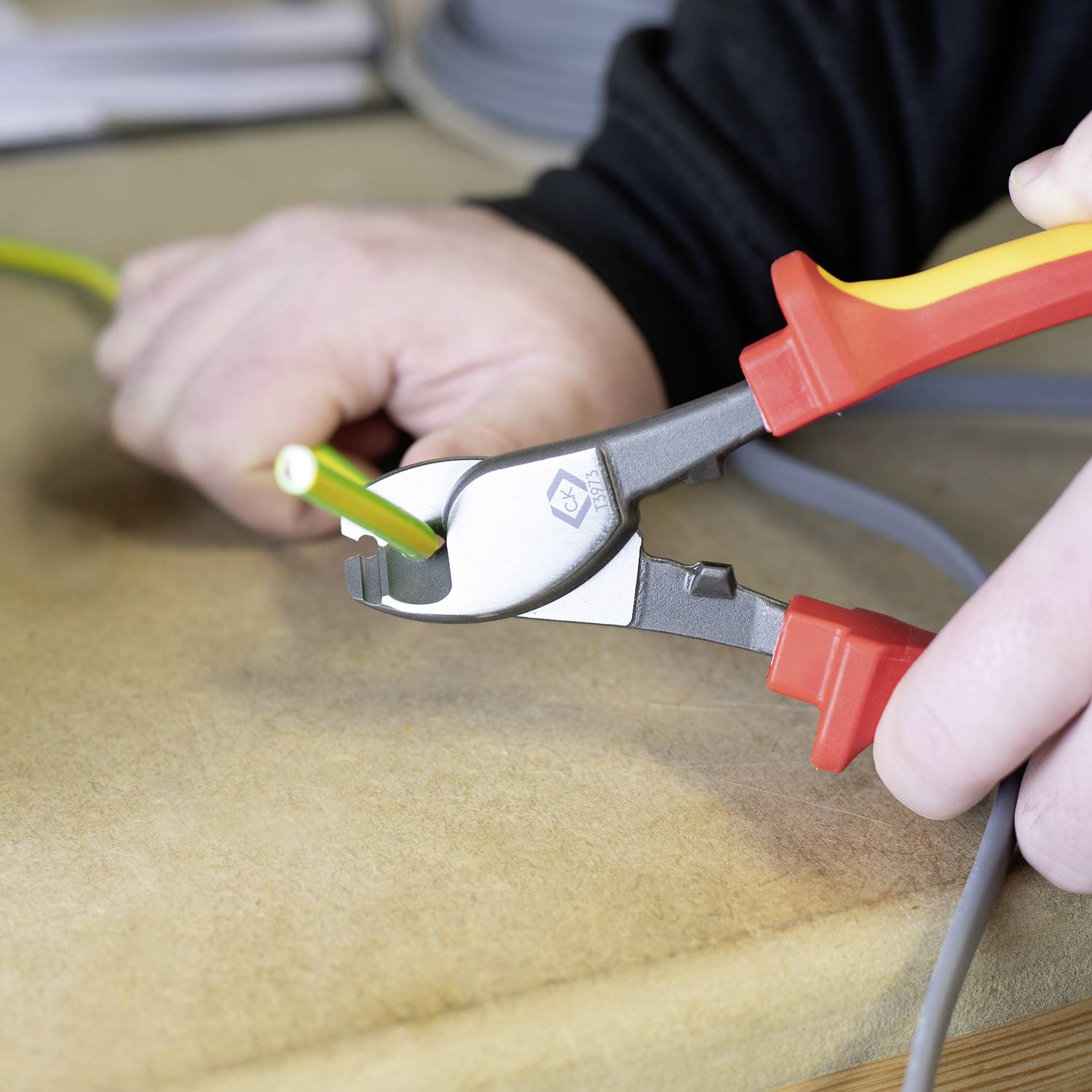 A person is cutting a yellow cable with a red cable cutter on a table. Hands and tools are in focus.