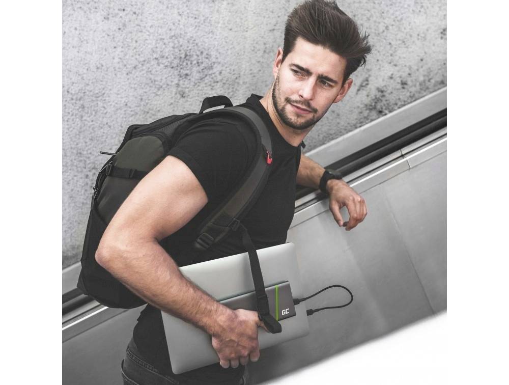 A man with a rucksack and laptop is standing on an escalator. He looks over his shoulder behind him.