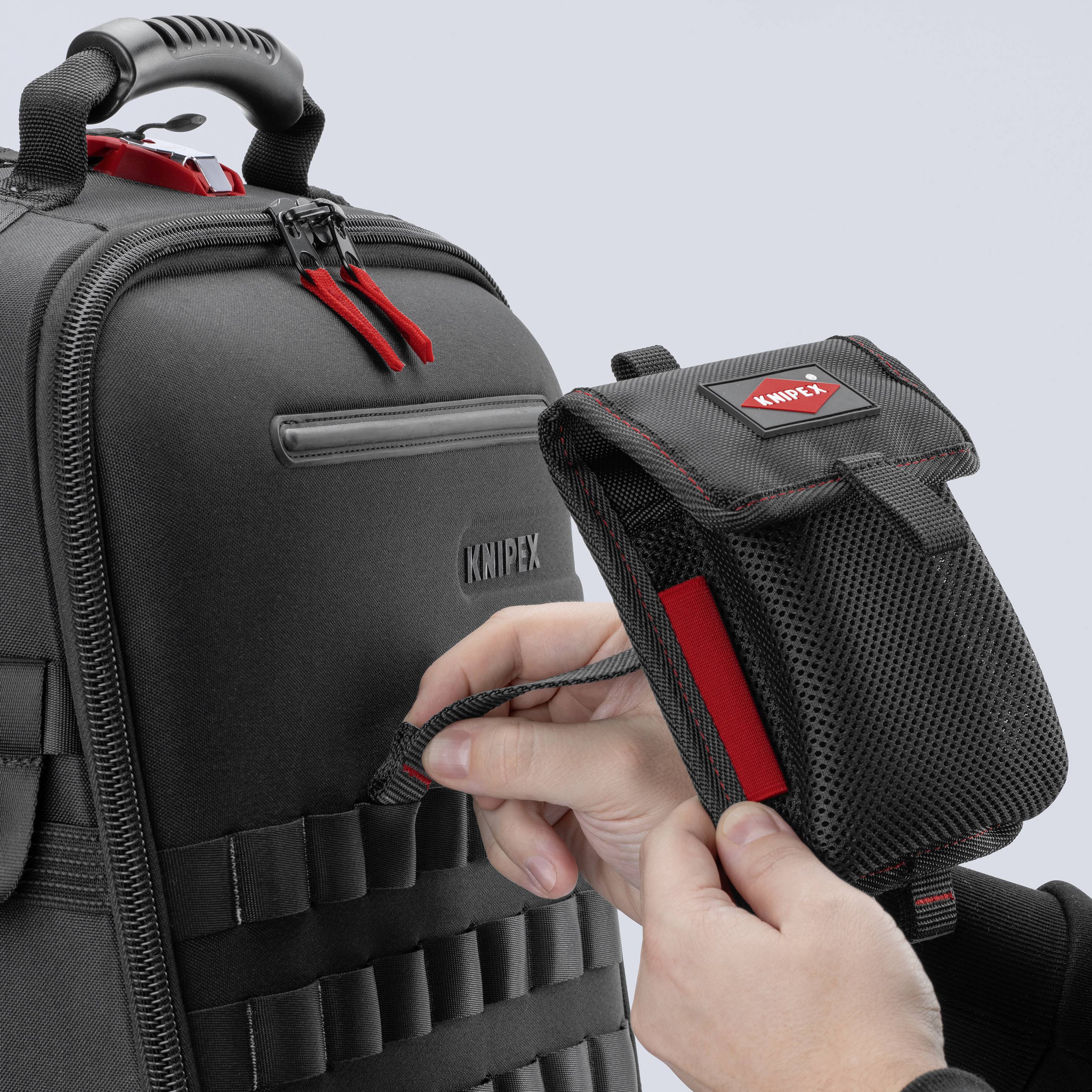 A hand pulls a small, black tool bag with a red Knipex logo from a large black rucksack.