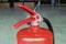 A red fire extinguisher with a secured lever stands on a greenish floor.