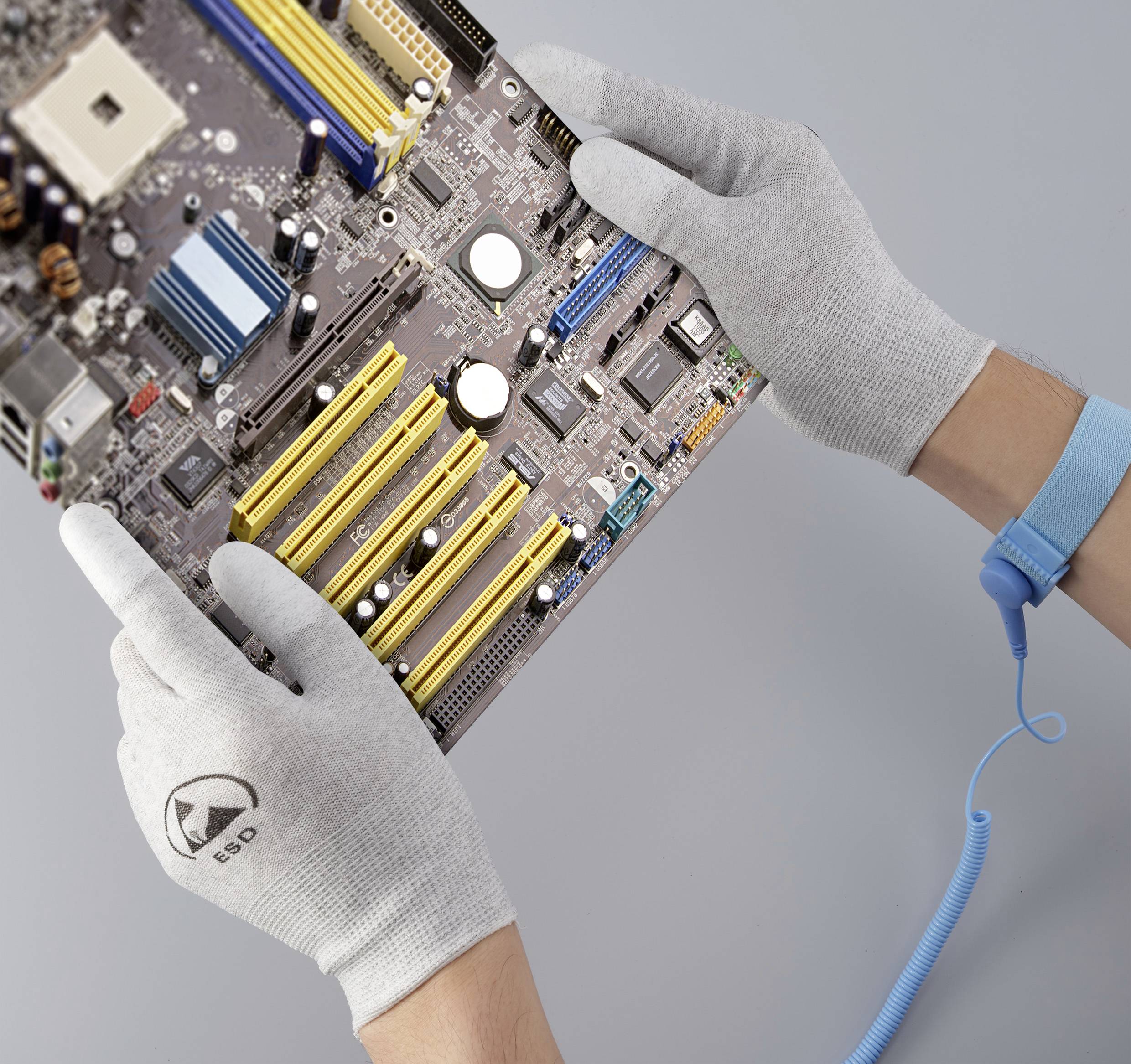 A pair of hands wearing ESD gloves are holding a circuit board, with an electrostatic protection wrist strap secured around the wrist.