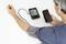 A man is measuring his blood pressure using a digital blood pressure monitor while holding a smartphone in his other hand.
