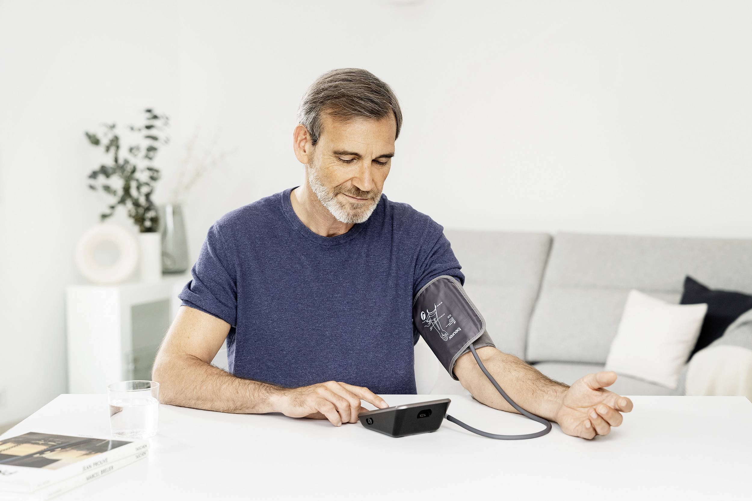 Medieval man measuring his blood pressure with a digital blood pressure monitor, sitting at a table in the living area.