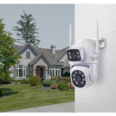 A security camera is mounted on a wall while it is raining. In the background, a house with a well-maintained garden can be seen.