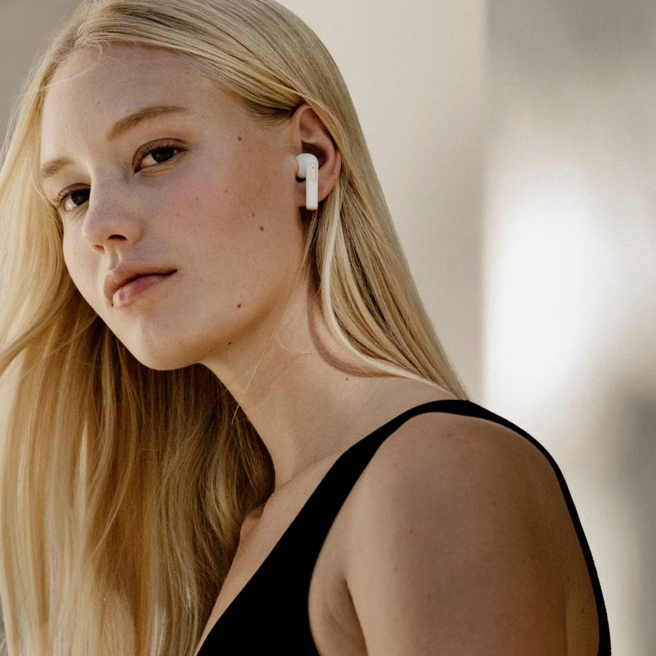 A woman with long blonde hair is wearing wireless earphones and looking to the side. Background out of focus.