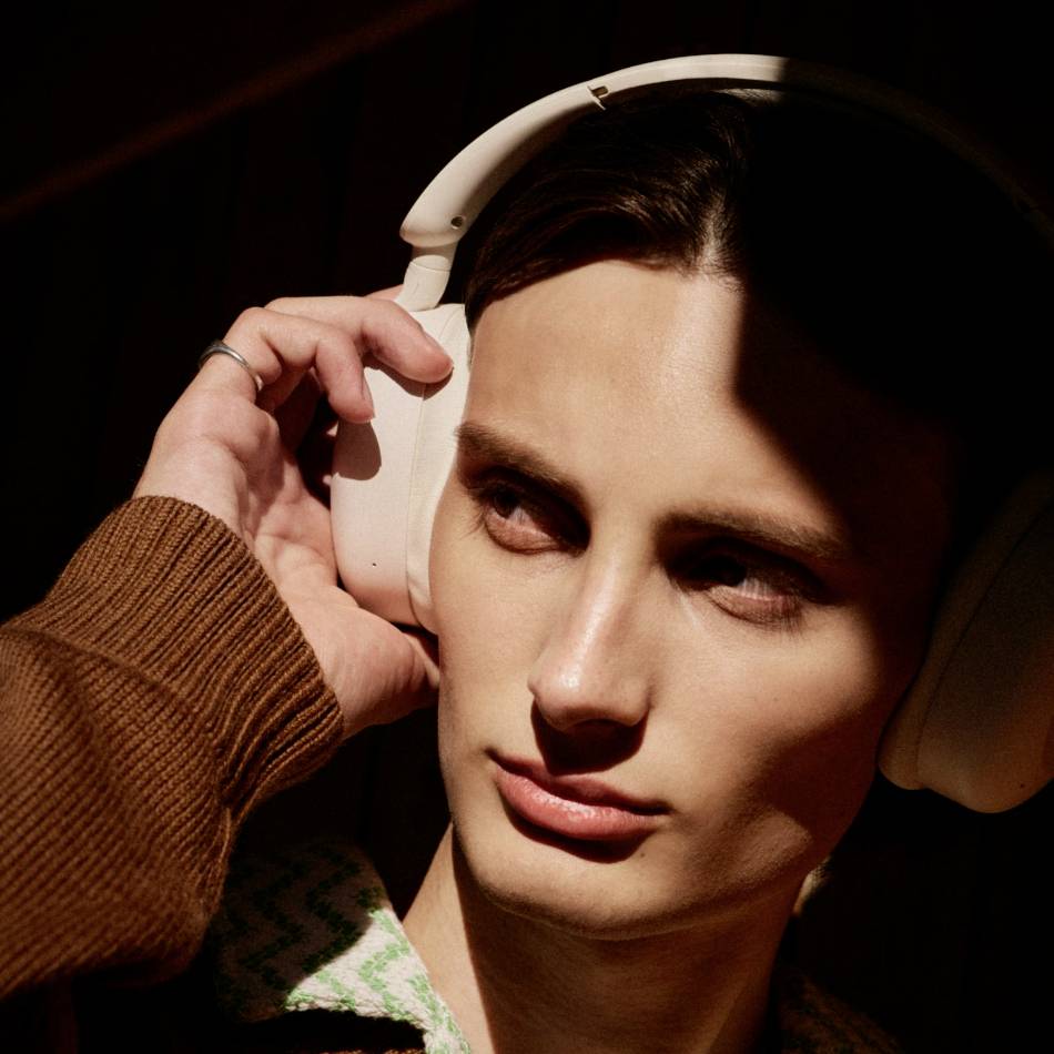 A person with white headphones is listening attentively. They have their hand slightly pressed against their ear, as if wanting to listen more closely.