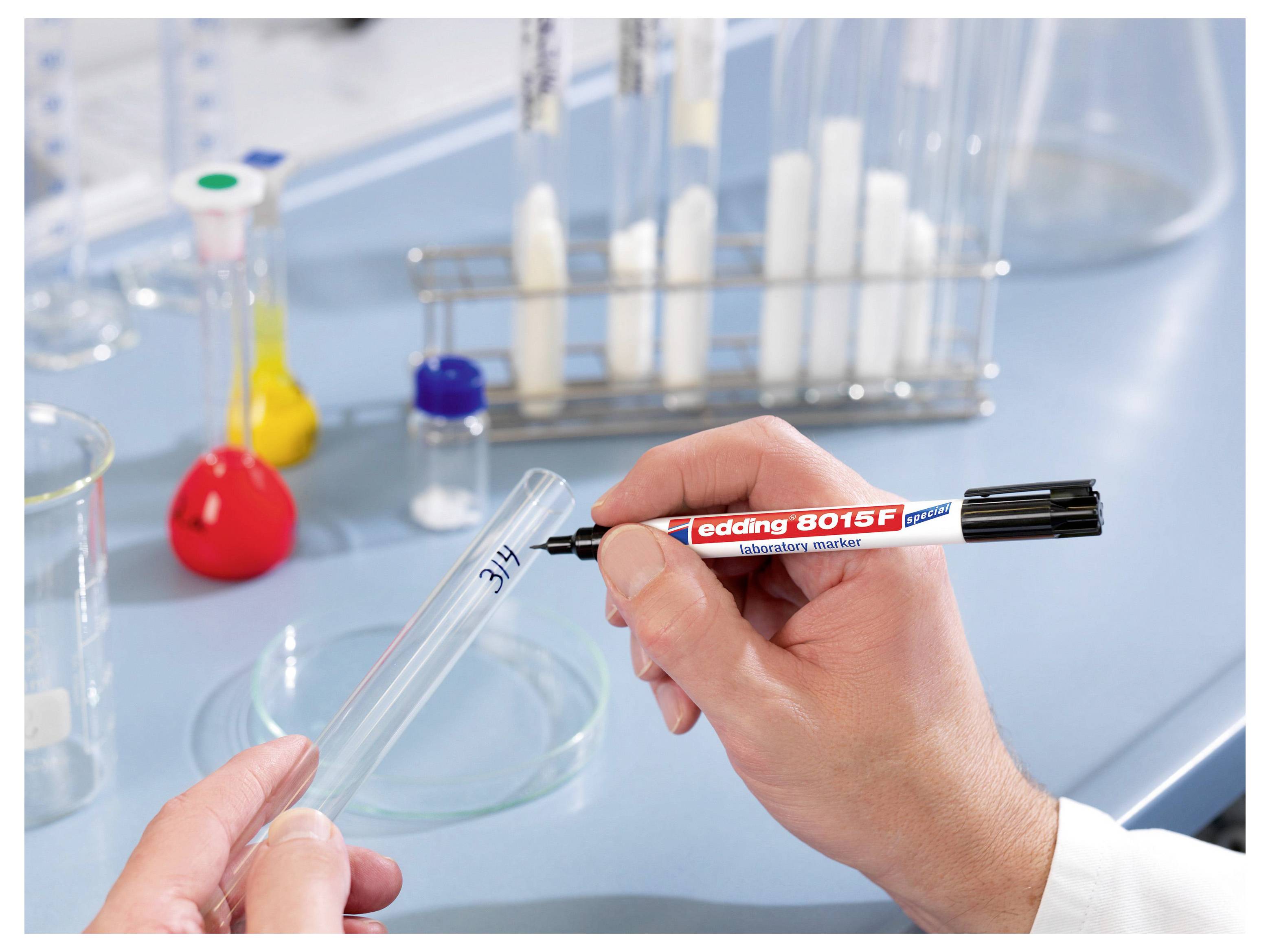 Hand labeling a test tube with a black permanent marker in a laboratory, with glassware and lab equipment in the background.