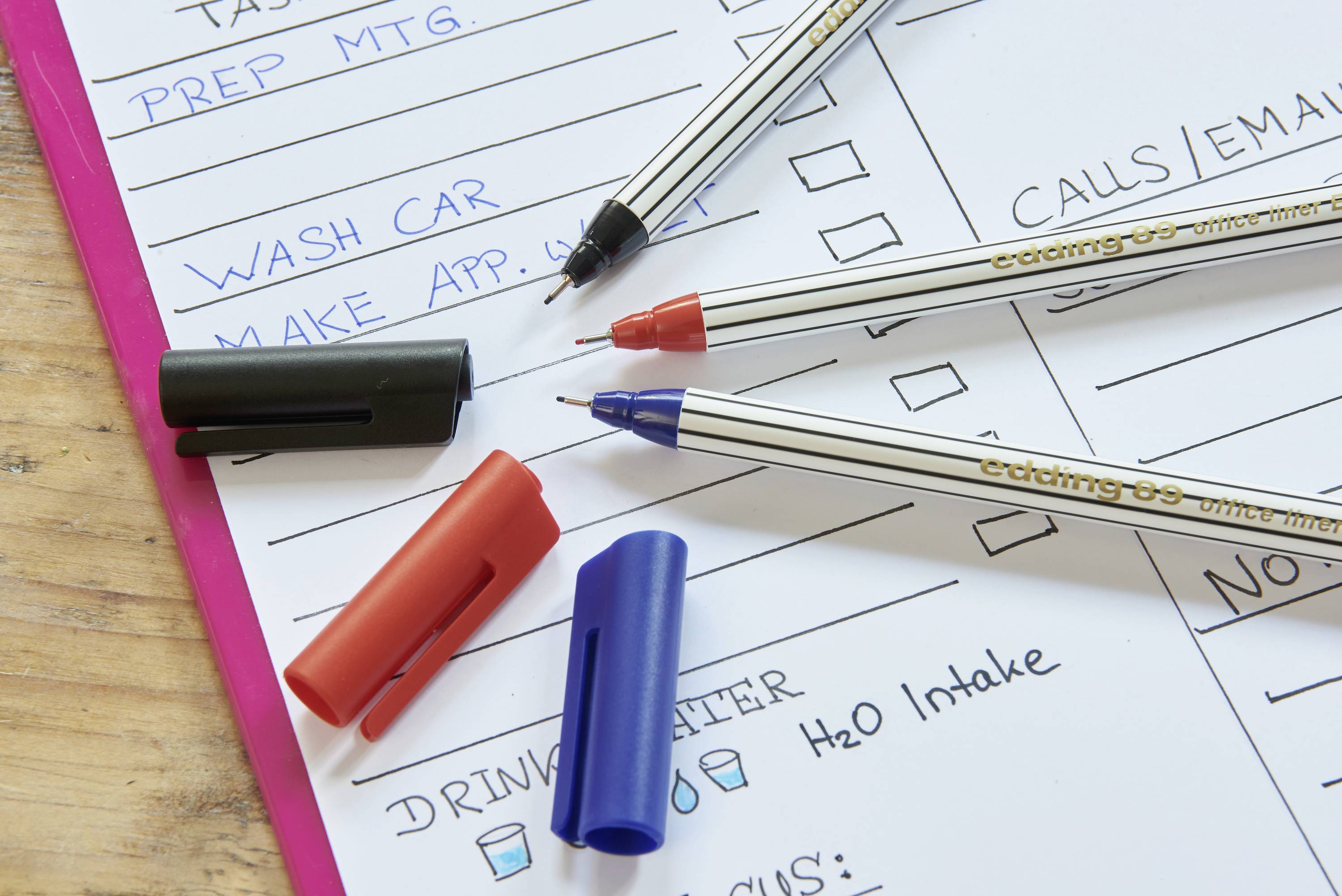 Three pens and their caps are lying on a to-do list. Tasks are written, including 'PREP MTG.' and 'WASH CAR'.