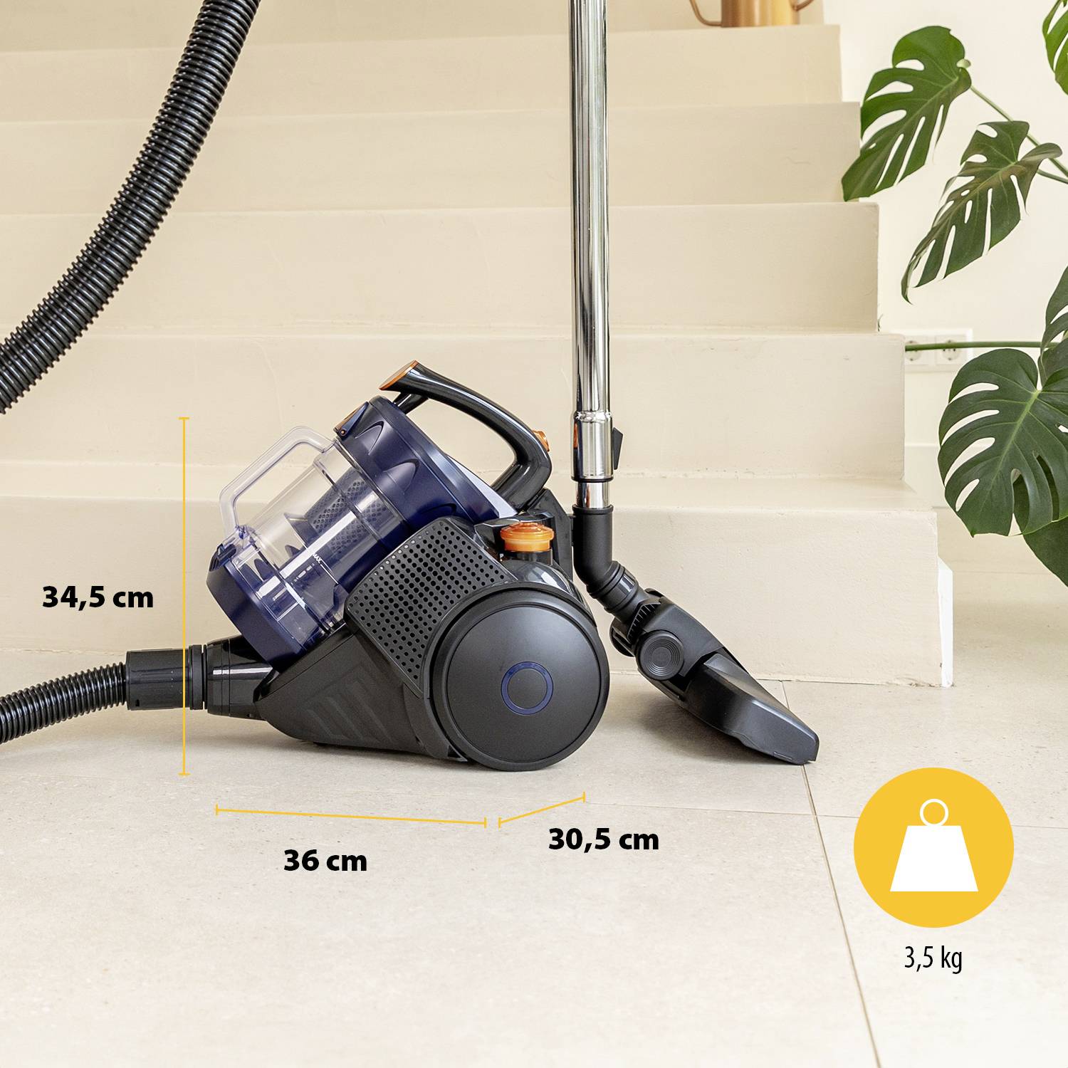 Vacuum cleaner with hose and accessories, standing on tiled floor in front of a staircase. Dimensions: 34.5 cm height, 36 cm depth, 30.5 cm width. Weight 3.5 kg.