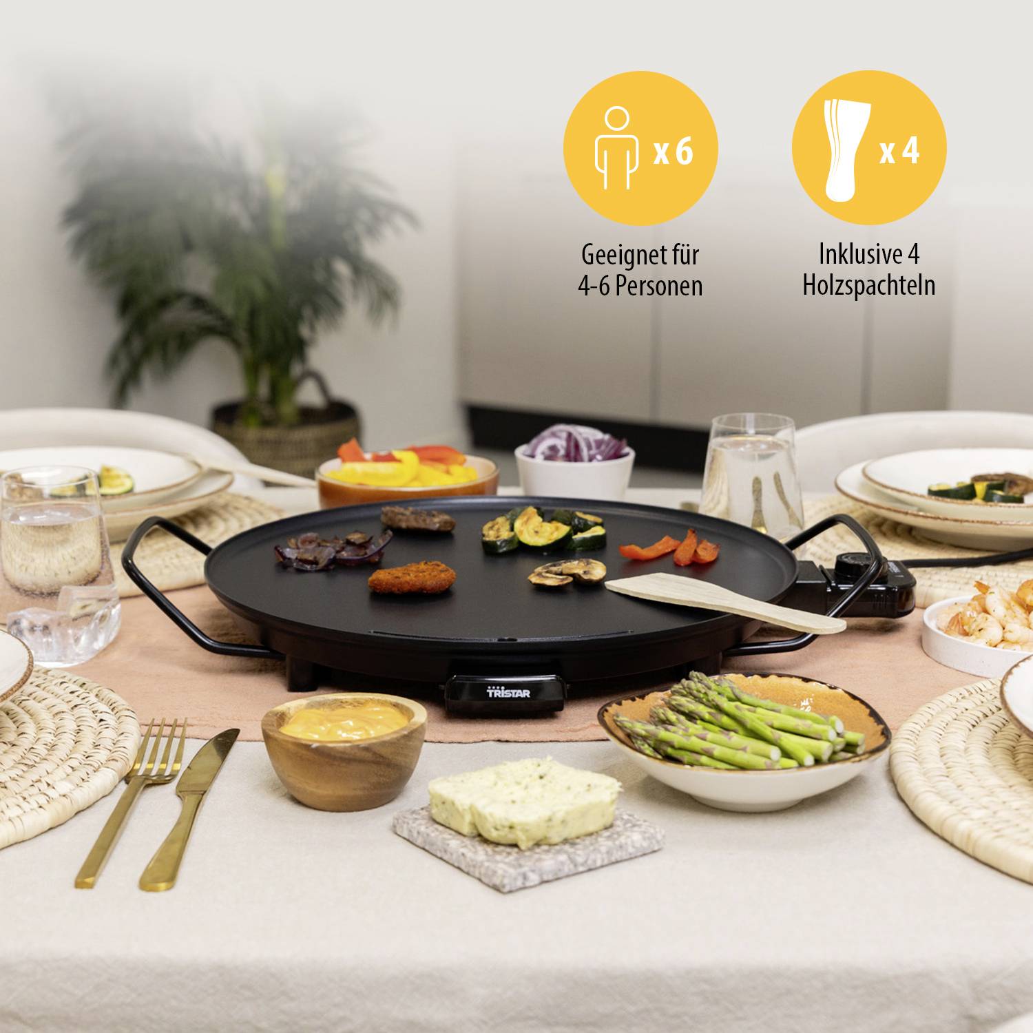 A table with laid plates, cutlery, dips and snack bowls surrounds an electric grill plate with vegetables. Suitable for 4-6 people.