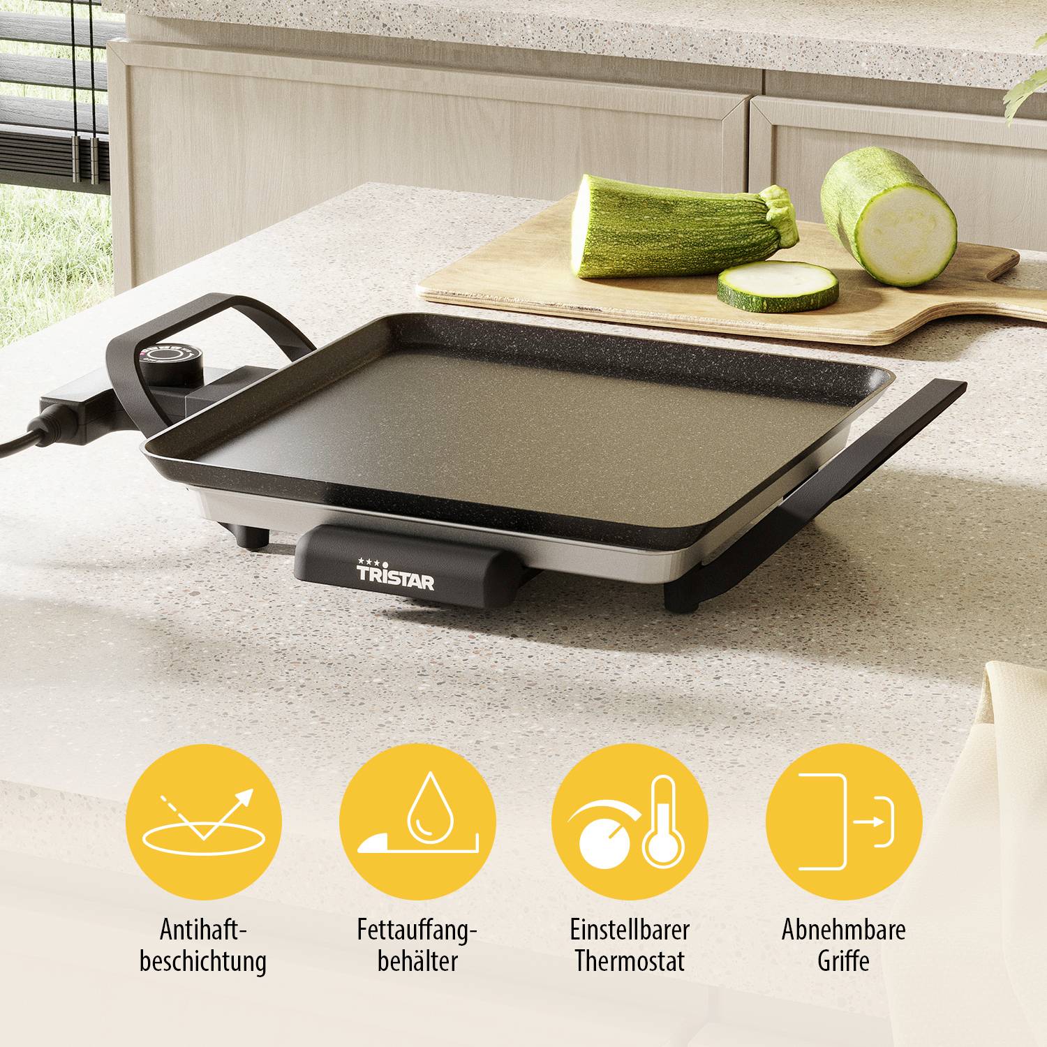 Electric griddle on a kitchen worktop, next to two courgettes. Features: non-stick coating, adjustable thermostat, removable handles.