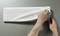 Two hands are peeling a transparent protective film from a white keyboard against a grey background.