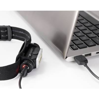 A head torch is connected to a laptop via a USB cable to be charged. The laptop is open.
