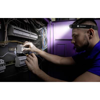 A technician is working with a head torch on an electrical cabinet, connecting cables to a circuit board. Electrical work in progress.