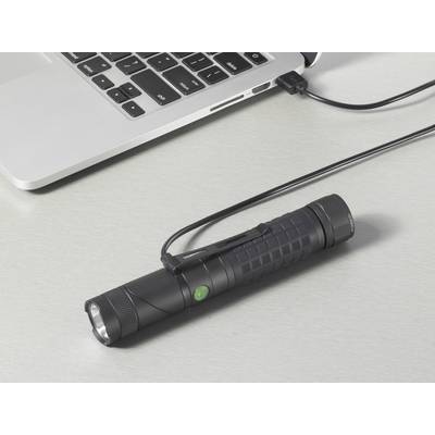 A torch with a USB cable is connected on a table next to a laptop.