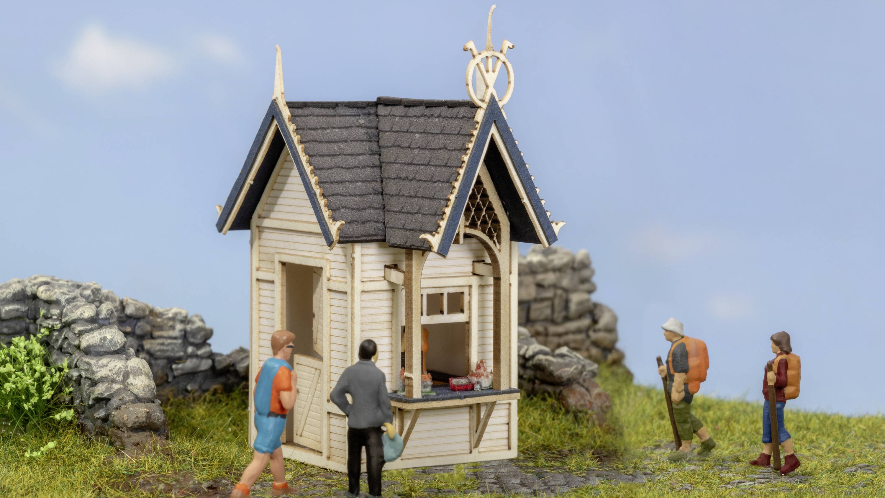 Miniature representation of a kiosk with four figures: Two hikers in outdoor clothing, one person in a suit, a holidaymaker in shorts.