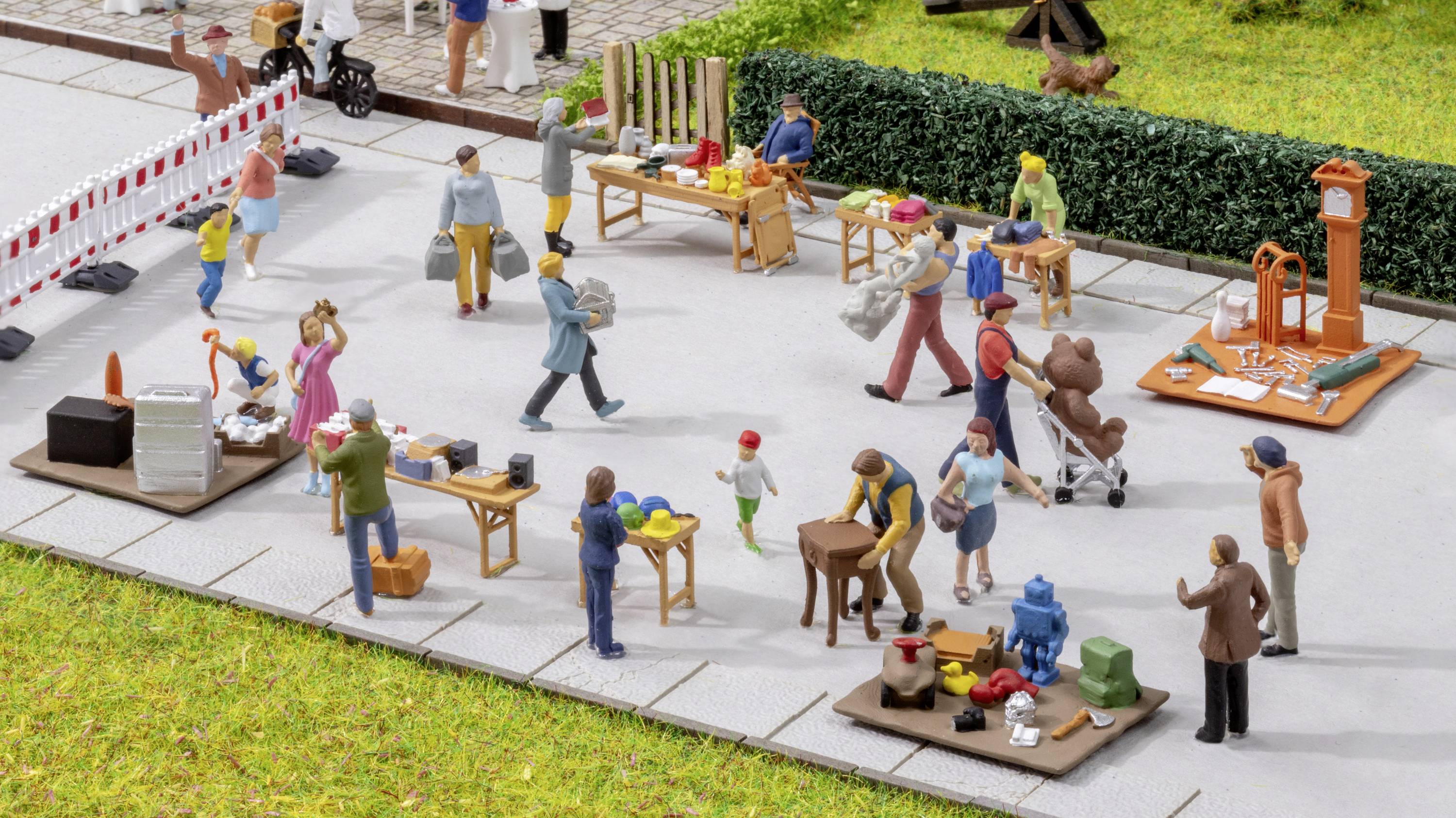 A model marketplace with miniature figures interacting at various stalls while shopping and selling goods.