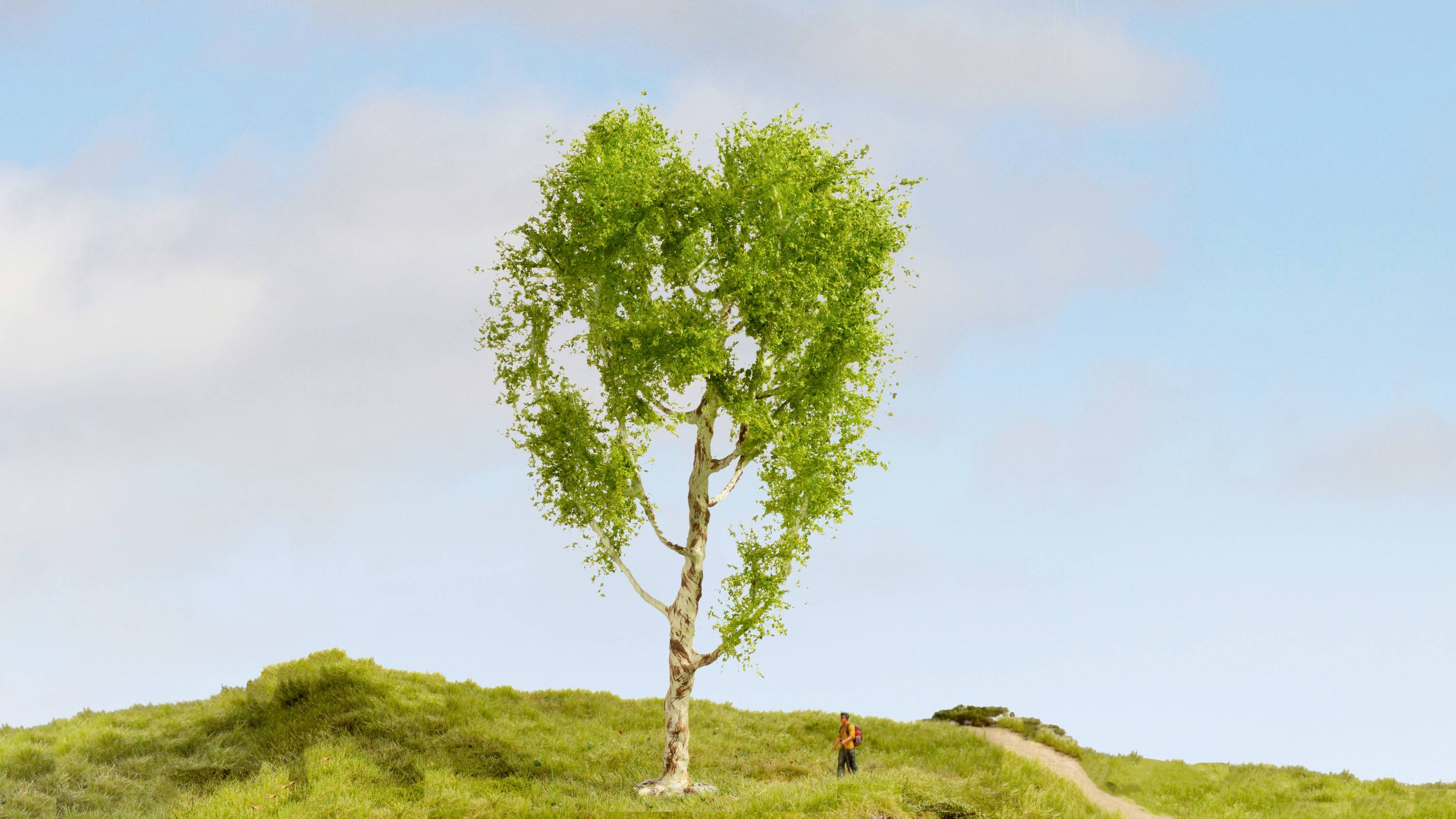 A heart-shaped tree stands alone on a green hill beneath a blue sky. A small figure walks along a path beside the tree.