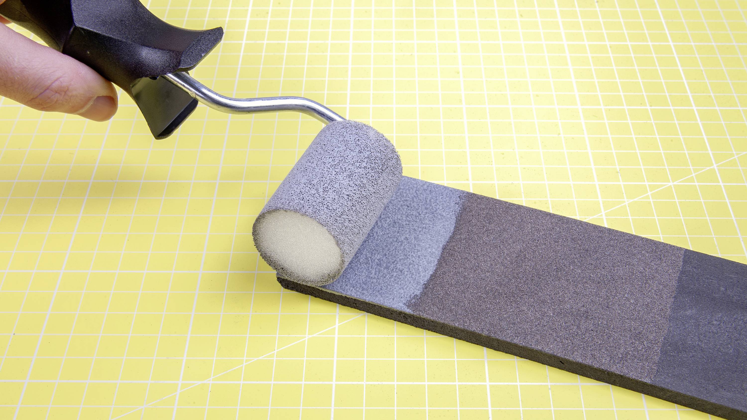 Painting a metal plate with a foam roller on a yellow grid background.