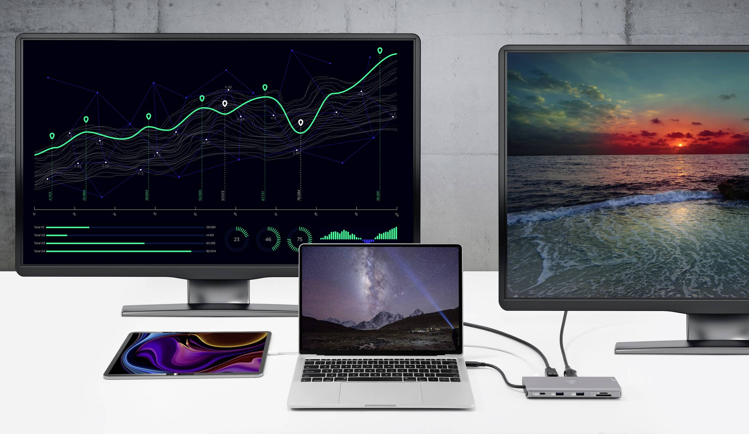 A laptop is connected between two larger monitors on a desk. The left monitor displays a diagram, the right monitor shows a sunset over the sea.