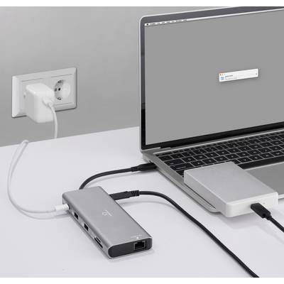 A laptop is connected to an external hard drive and a power socket via a USB-C hub and multiple cables. A pop-up is visible on the display.