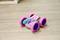 A colourful toy car with four large, pink tyres sits on a wooden floor. It has a striking, vibrant design.