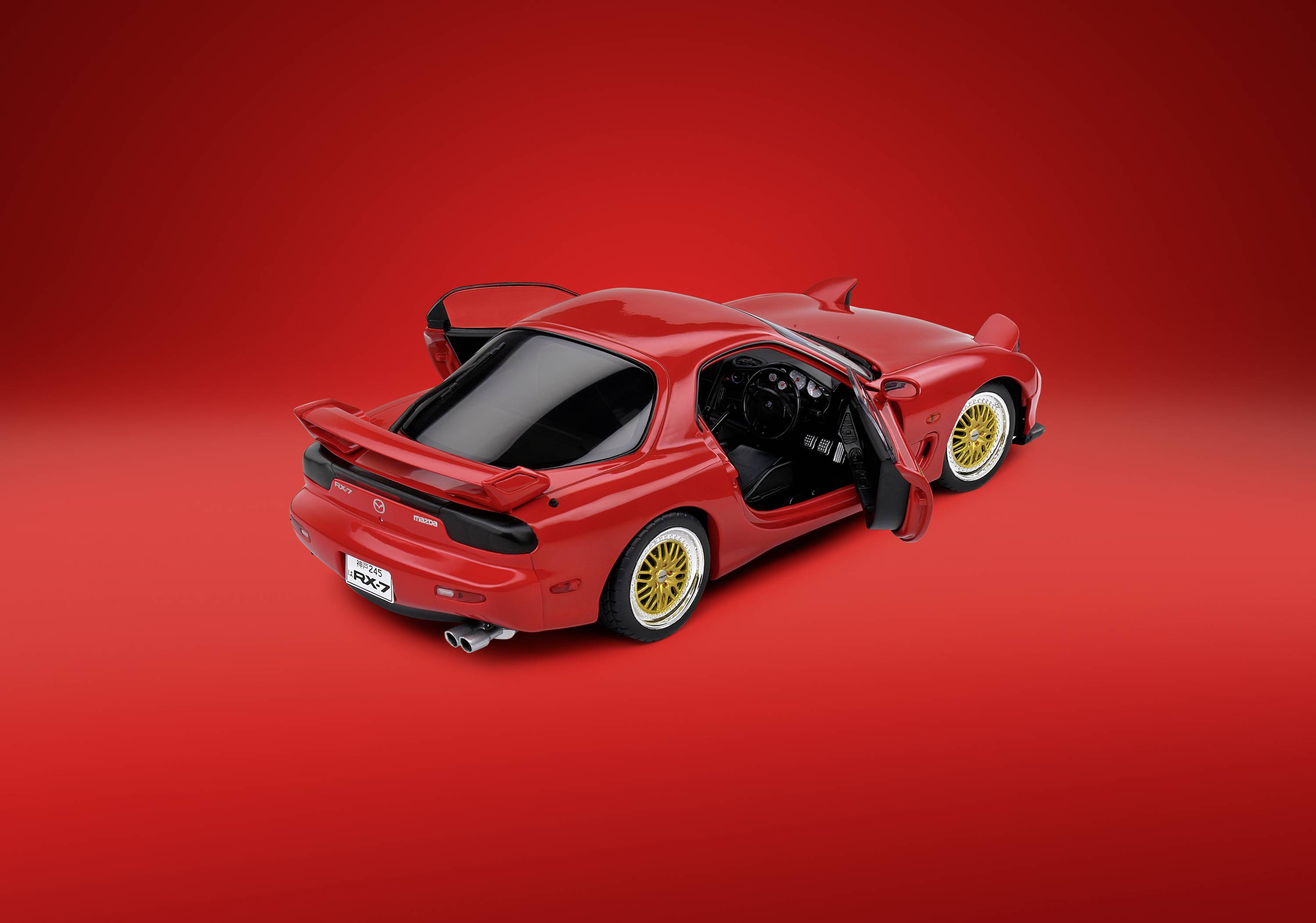 Red sports car with open doors against a red background. Gold-coloured alloy wheels and a spoiler stand out from the glossy paintwork.