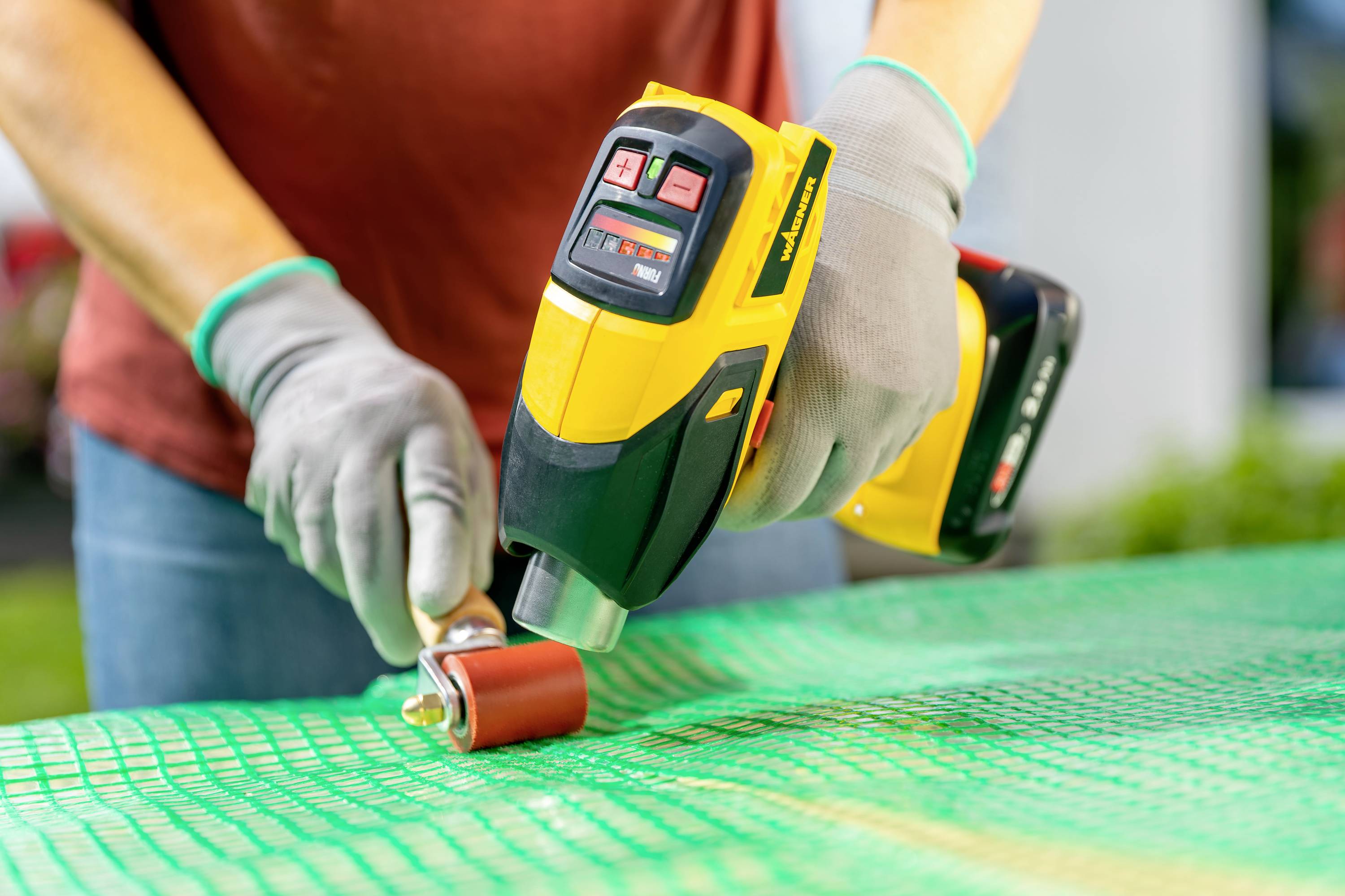 A person is repairing a plastic surface using a heat gun and roller. Hands are wearing gloves.