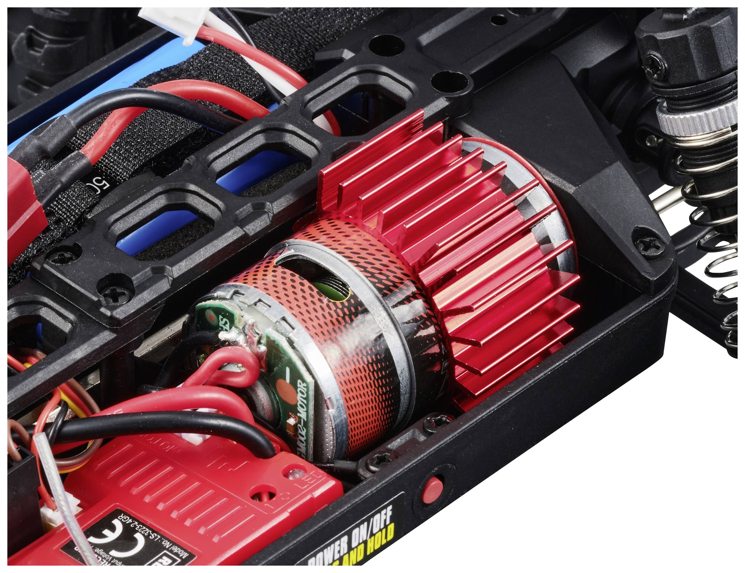 A red electric motor with cooling fins is installed in an RC model. Several cables are connected to it.