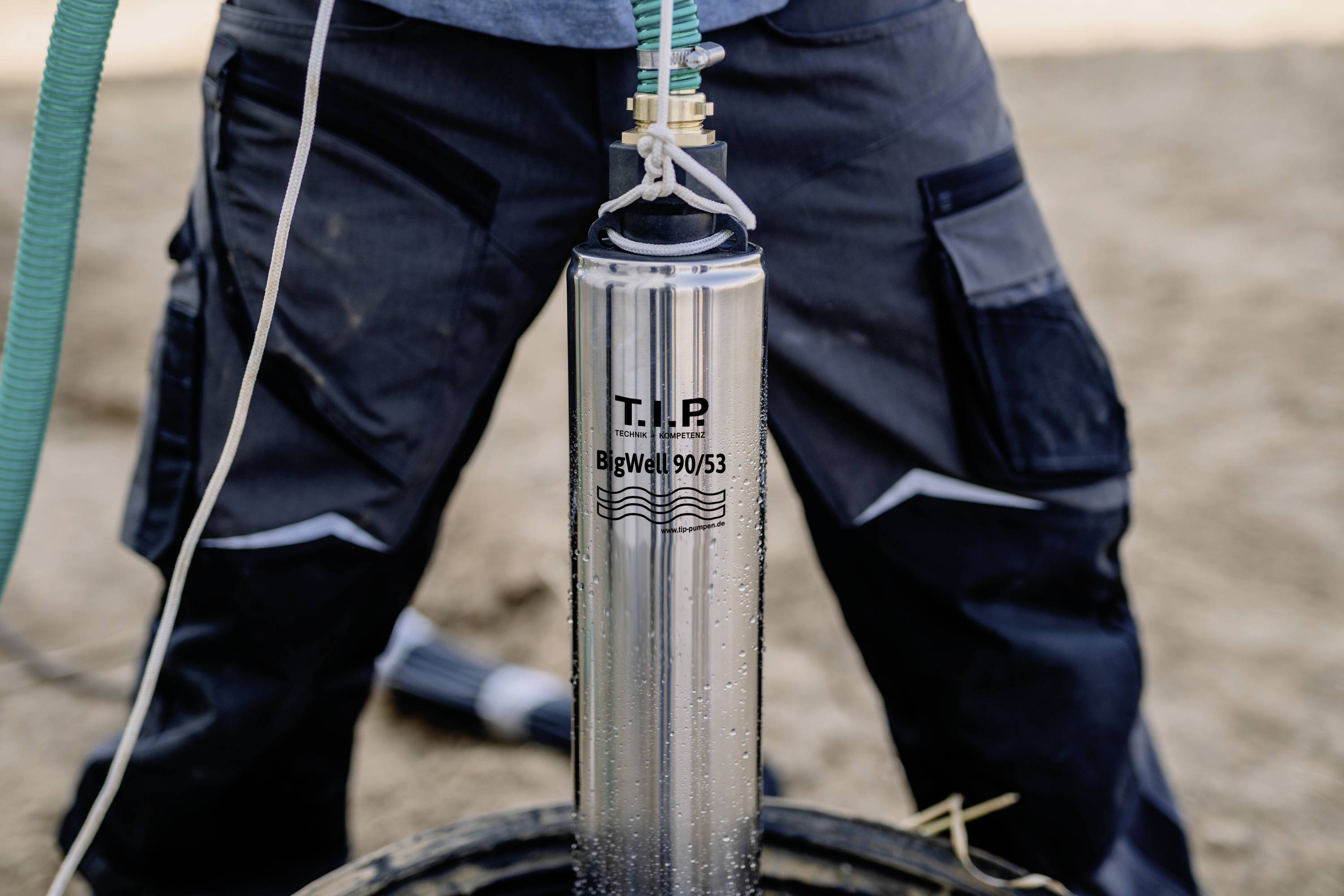 A person operating a water pump from the brand 'T.I.P.'. The silver device is being handled professionally.