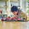 A child is playing intently with a train toy on a table in a living room. Bookshelves are visible in the background.