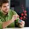 A man arranges flowers from a cherry blossom bonsai in a small blue pot. He is smiling and wearing a green shirt.