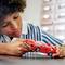 A child plays intently with a red toy car on a table. They are wearing a blue striped jumper.