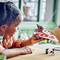 A child is playing with a homemade toy spaceship made from Lego bricks. A small Lego figurine stands beside it on the table.