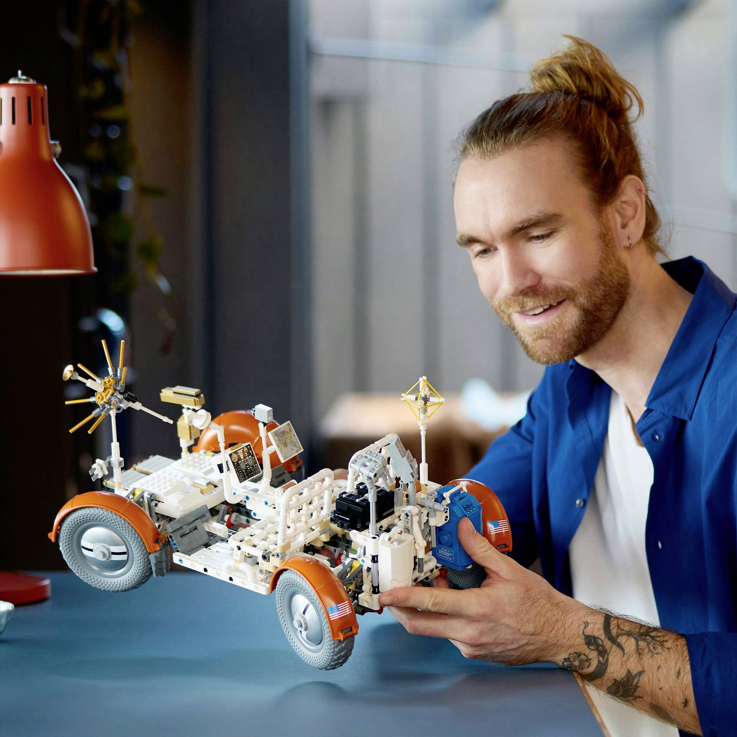 A smiling man is building a model car from Lego. The car is intricately designed with orange and white pieces.