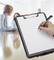 A hand is writing on a clipboard with white paper, with three people blurred in a meeting in the background.