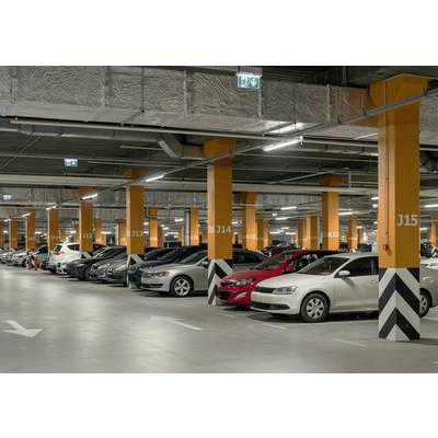 A spacious, well-lit parking area in a multi-storey car park. Various cars are parked side by side between orange-marked columns.