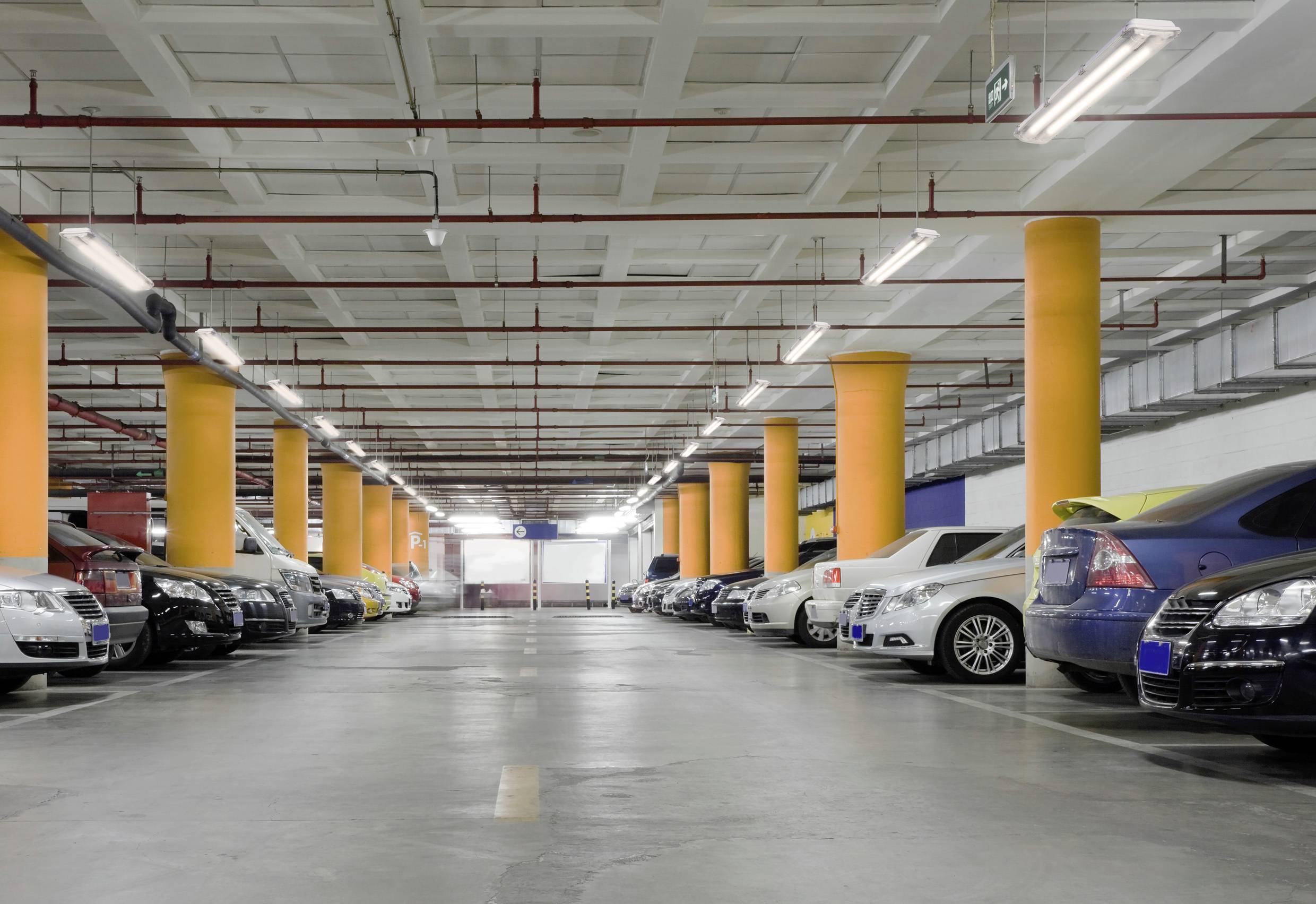 A multi-storey car park with cars parked on both sides. Bright lighting and yellow pillars can be seen.