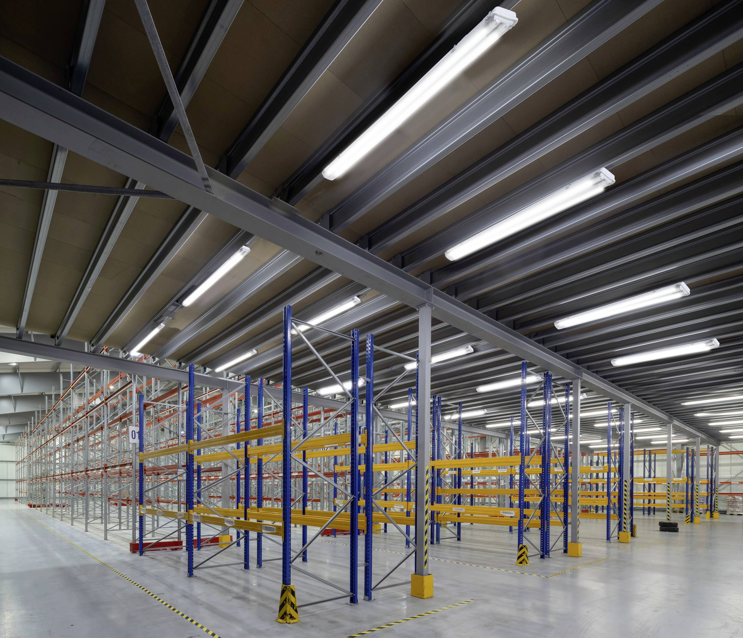 Empty warehouse with tall shelving; no products stored; lighting from LED fixtures on the ceiling; yellow safety markings on the floor.