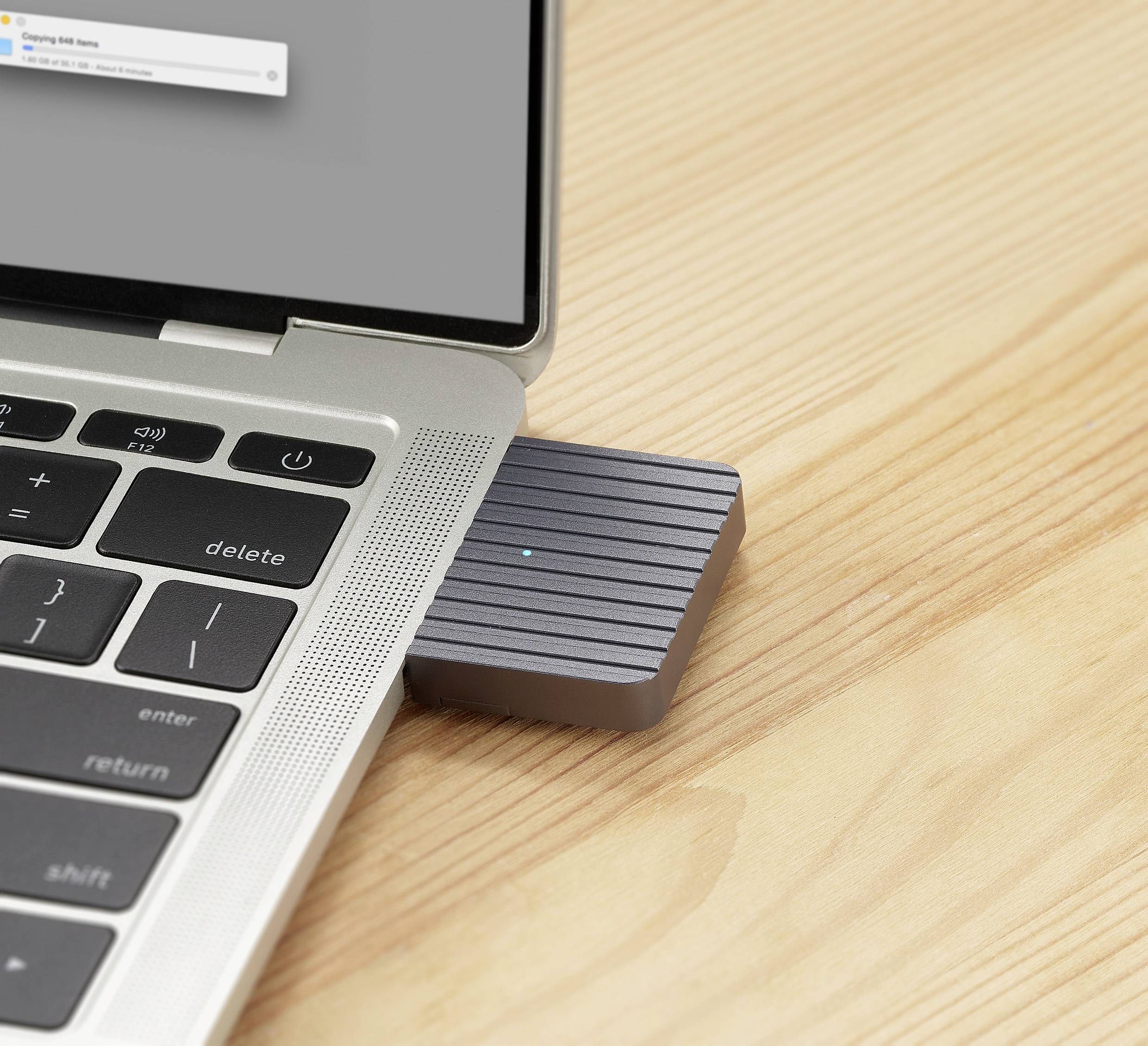 Laptop with a USB memory stick inserted on the left side. Focus is on the connection between laptop and device on a wooden table.