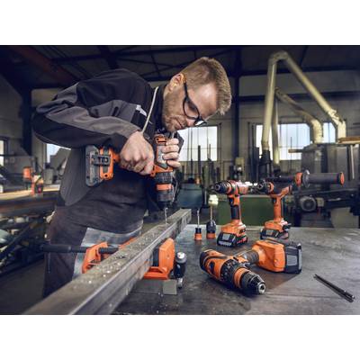 A man wearing work attire is using a drill to machine a piece of metal in a metalworking workshop.