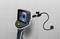 Endoscope camera with a flexible swan-neck reveals the screen content of a dark tube. Grey tiles in the background.