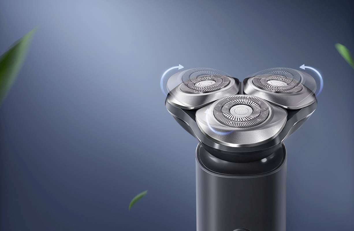 Electric razor with three rotating cutting heads, surrounded by green leaves on a blue background.