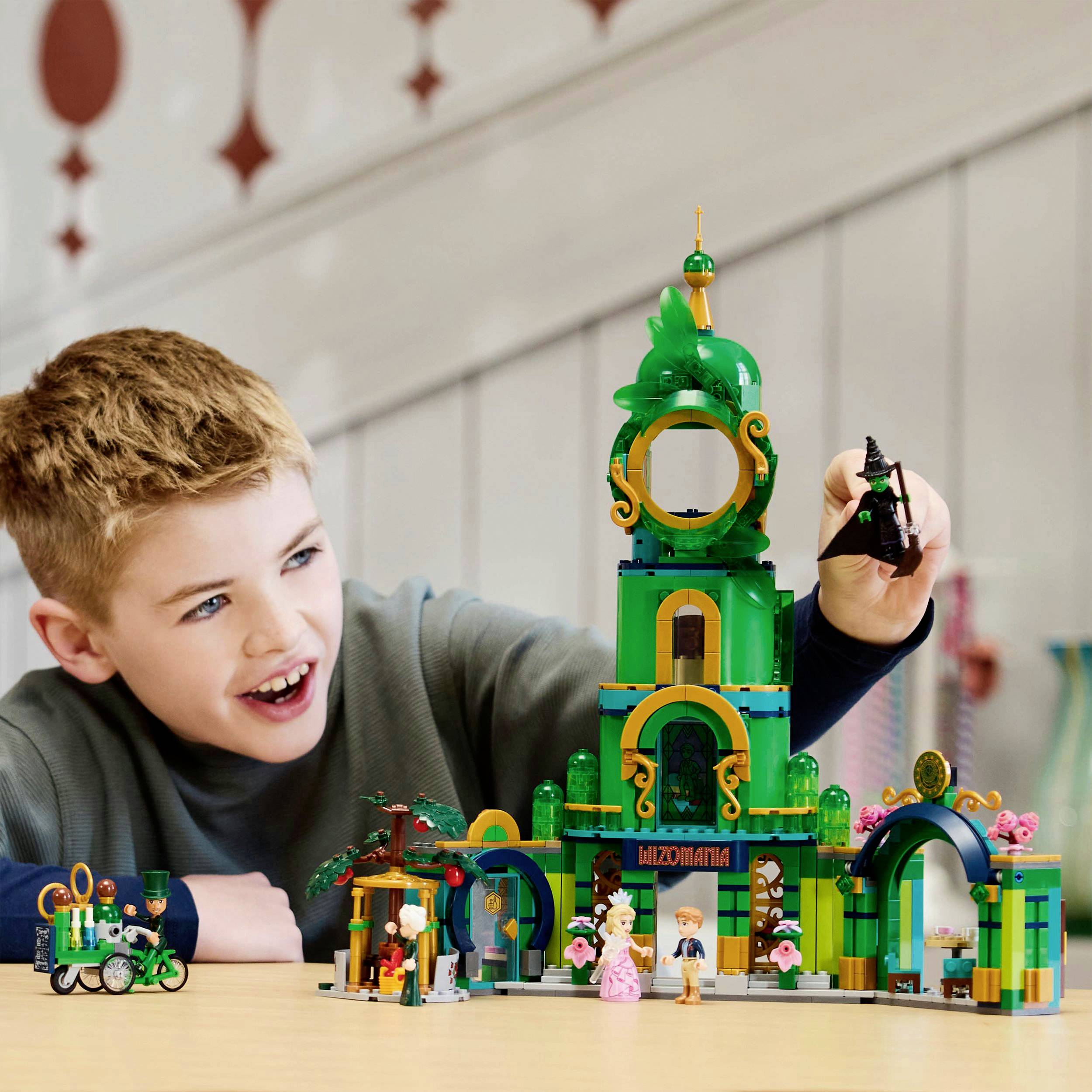 A child plays with a colourful building block set, forming a tall tower. They hold a black figurine and smile.