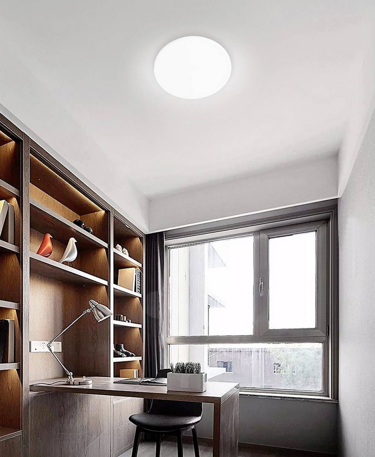 A modern home office with wooden shelves, a desk, lamp, and a window with an outside view. Shelves contain decorative objects.